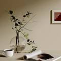 Transparent Glass Vase with Green Leaves and White Coffee Cup Open Magazine on Neutral Table