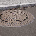 Urban Road Facilities Circular Manhole Cover on Asphalt Surface with Cobblestone Pavement and Curb