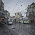 Bustling Commercial Street With Passing Tram Historic Buildings Wet Pavement And Street Lamps