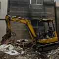 KOMATSU Yellow Excavator Engaged In Demolition Work Amidst Rubble And Old Buildings