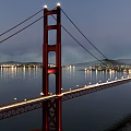 Red Suspension Bridge Illuminated Over Calm Water With City Lights At Night