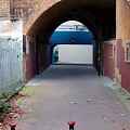 Brick Archway Passageway Featuring Walls Wooden Fence Leaves Trash Blue White Wall Clock Red Bollards
