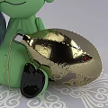 Green Doll With Black Feet Holding Purple Metallic Decorative Ball On White Patterned Background