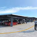 Covered Parking Lot with Parked Cars Yellow Lines and People Walking Under Blue Sky