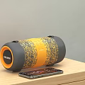 MOVIN Bluetooth Speaker Orange Grey Woven Cylindrical Design With Smartphone On Wooden Table