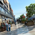 Vibrant Commercial Street with Shops Sunshades Pedestrians Trees Flower Boxes and Paved Ground