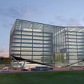 Modern Office Building With Curved Glass Curtain Wall Green Lawn And Parked Vehicles At Twilight