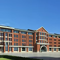 Red Brick School Building Featuring Arched Entrance Large Windows and Green Lawn Against Blue Sky