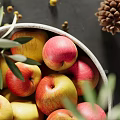 Ceramic Bowl Filled With Fresh Apples And Olive Branches On Dark Countertop With Pine Cone Nearby