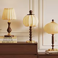 Three Table Lamps With Wooden Bases And Lampshades On Cabinet With Books And Green Plant