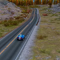 Blue Car Driving on Winding Road Through Grassland Hills and Trees