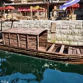 Traditional Wooden Boat Moored by Riverside with Stone Wall and Colorful Canopies