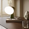 Green Table Lamp Illuminates On Books With Small Cup And Stone Near Window Blinds