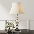 Ivory Lampshade Table Lamp with Glass Globe Base and Green Plant against White Wall Paneling