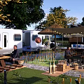 Scenic Campsite With Camper Van Tents Shade Umbrellas Wooden Tables Surrounding Trees And Green Grass