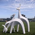 Group of White Deer Sculptures on Green Grass with City Skyline and Blue Sky
