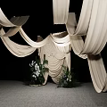 Stylish Floral Display Featuring White Draped Fabric And Central Decorative Greenery On Gray Floor