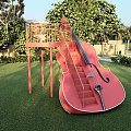 Scenic View of Giant Pink Cello Structure With Staircase on Lush Green Lawn and Trees