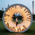 Illuminated Circular Landscape Sculpture With City Skyline Silhouettes And Person In Urban Park