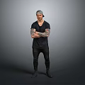 Tattooed Man Wearing Black T Shirt And Pants With Arms Crossed Against Gray Background