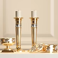Two Elegant Golden Candle Holders With Small Golden Bowl And Dishes On Light Colored Wall Background