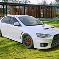 White Mitsubishi Sports Sedan With Rear Spoiler Alloy Wheels On Green Grass Wooden Structure Background