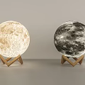 Two Moon Lamps Featuring Lunar Surface Texture And Wooden Triangle Stand In Light Dark Shades