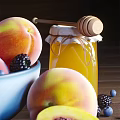 Fresh Ripe Peaches in Blue Bowl with Blackberries Blueberries and Honey Jar on Wooden Table