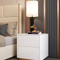White Bedside Table with Lamp Books and Golden Ornament beside Beige Upholstered Headboard Bed
