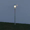 Outdoor Light with Silver Pole and White Lampshade Illuminated in Grass Field under Blue Sky