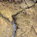 Scenic Mountainous Terrain With Flowing Stream Yellowish Green Textured Slopes And Visible Cracks