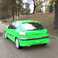 Green Hatchback Car Parked On Roadside With Trees Autumn Leaves And Park Background