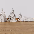 Carved Buddha Sculptures In Three Different Poses On Wooden Floor Against White Wall