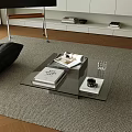Modern Glass Coffee Table On Rug With Books Cup And Black Chair In Living Room