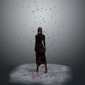 A woman in black standing with red petals falling around on gray background under spotlight