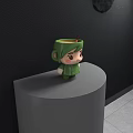 Green Cartoon Character Shaped Mug On Gray Round Platform With Black Wall And Brown Stirrer