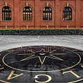 Circular Garden Ornament With Trimmed Hedges And Arched Red Brick Building Background
