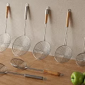 Stainless Steel Skimmers With Wooden Handles Hanging On Wall And On Countertop With Green Apples