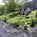 Tranquil Courtyard Garden With Green Plants Stones Path Lanterns Statues And Black Wall