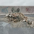 Stones and Wood Debris Pile Against Graffiti Covered Concrete Wall