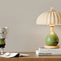 Green Table Lamp With Pleated Beige Lampshade On Stacked Books And Decorative Doll