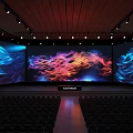 Large Stage With Three Screens Displaying Colorful Flowing Patterns And Auditorium Seats