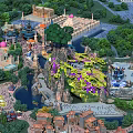 Amusement Park Featuring Mountain Structure Colorful Decorations Water Area Trees Buildings and Crowded Visitors