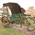 Traditional Green Rickshaw With Red Seats And Black Canopy Near Brick Wall
