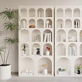 Double White Display Cabinet With Arched Compartments Holding Ornaments Books Vases Beside Tall Potted Plant