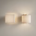 Two Wall Lamps With Square And Round Fabric Shades On Light Wall Emitting Soft Glow