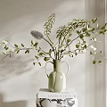 Light Green Vase with Green Leaves and Feathery Decor on Patterned Book in Soft Light