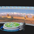 Circular Display Cabinet With Green Model Standing Person And Curved Screen Displaying Snowy Mountain Ancient Architecture