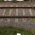 Old Train Tracks With Weathered Wooden Sleepers Gravel And Overgrown Grass In Rural Area