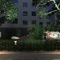 Commercial Street Night View With Lush Green Plants Surrounding Modern Buildings And Warm Lighting